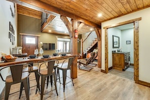 A spacious kitchen with a wooden ceiling, a dining area with bar stools, and a staircase leading to another level.