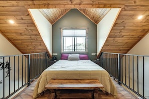 A bedroom with a sloped ceiling, a bed, a window, and a bench.