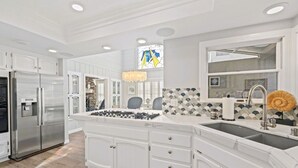 A modern kitchen with white cabinetry, a stainless steel refrigerator, a gas stove, and a large window with a stained glass design.