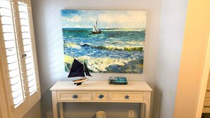 A bedroom with a bed, a desk with a sailboat model, a painting of a sailboat on the wall, and a window with blinds.
