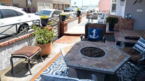 A patio with outdoor seating, a fire pit, and a view of parked cars and buildings.