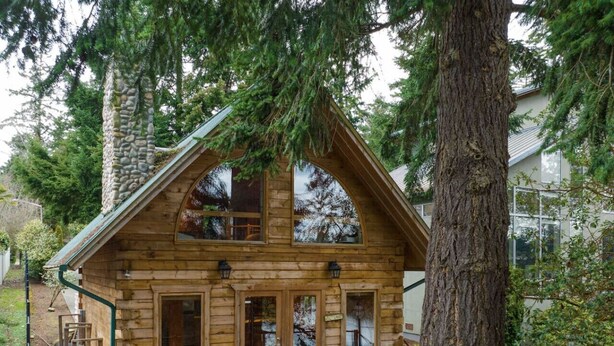 Una cabaña de madera con porche, ventanas amplias y una chimenea de piedra.