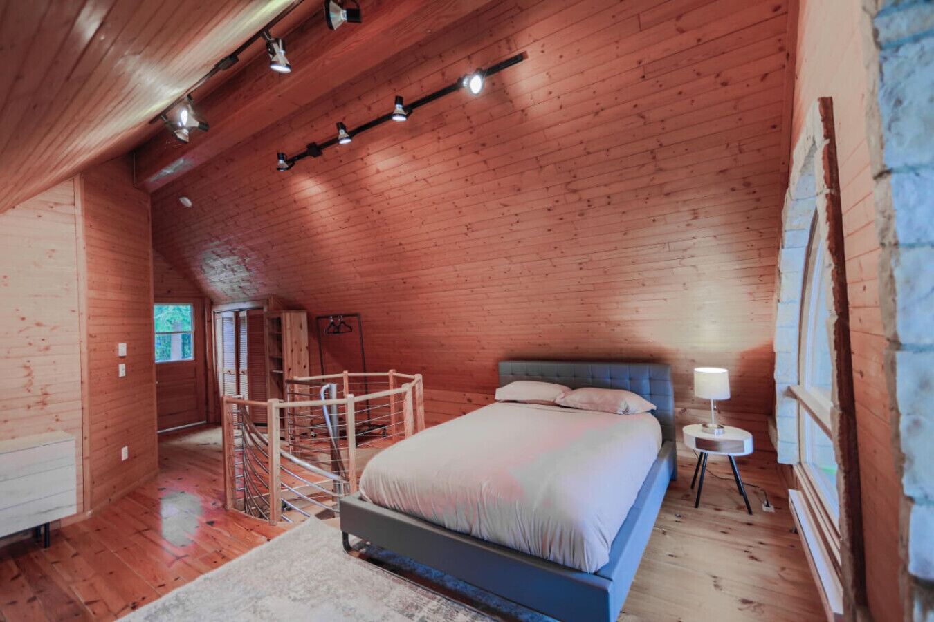 A wooden cabin bedroom with a bed, a small bedside table, and a window.