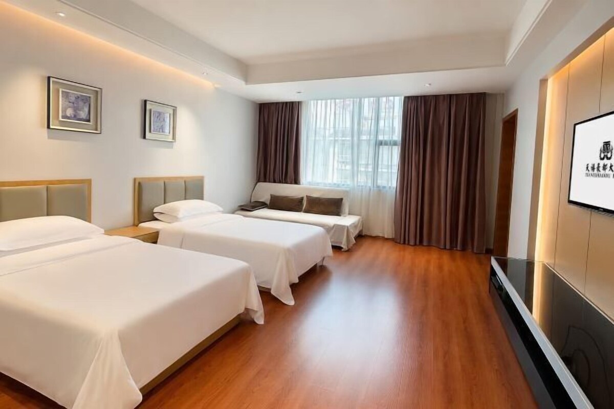 A hotel room with two beds, a flat-screen TV, and a large window with curtains.
