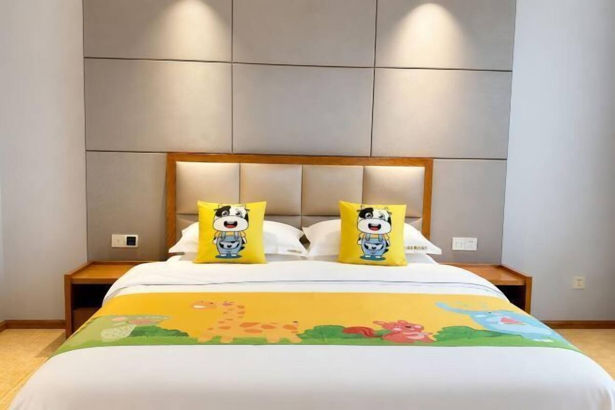 Een hotelkamer met een bed, twee kussens met tekenfilmfiguren, een nachtkastje en een bedtafel.