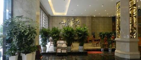 Un vestíbulo con suelo de mármol, plantas en macetas, un mostrador de recepción y una pared decorativa.