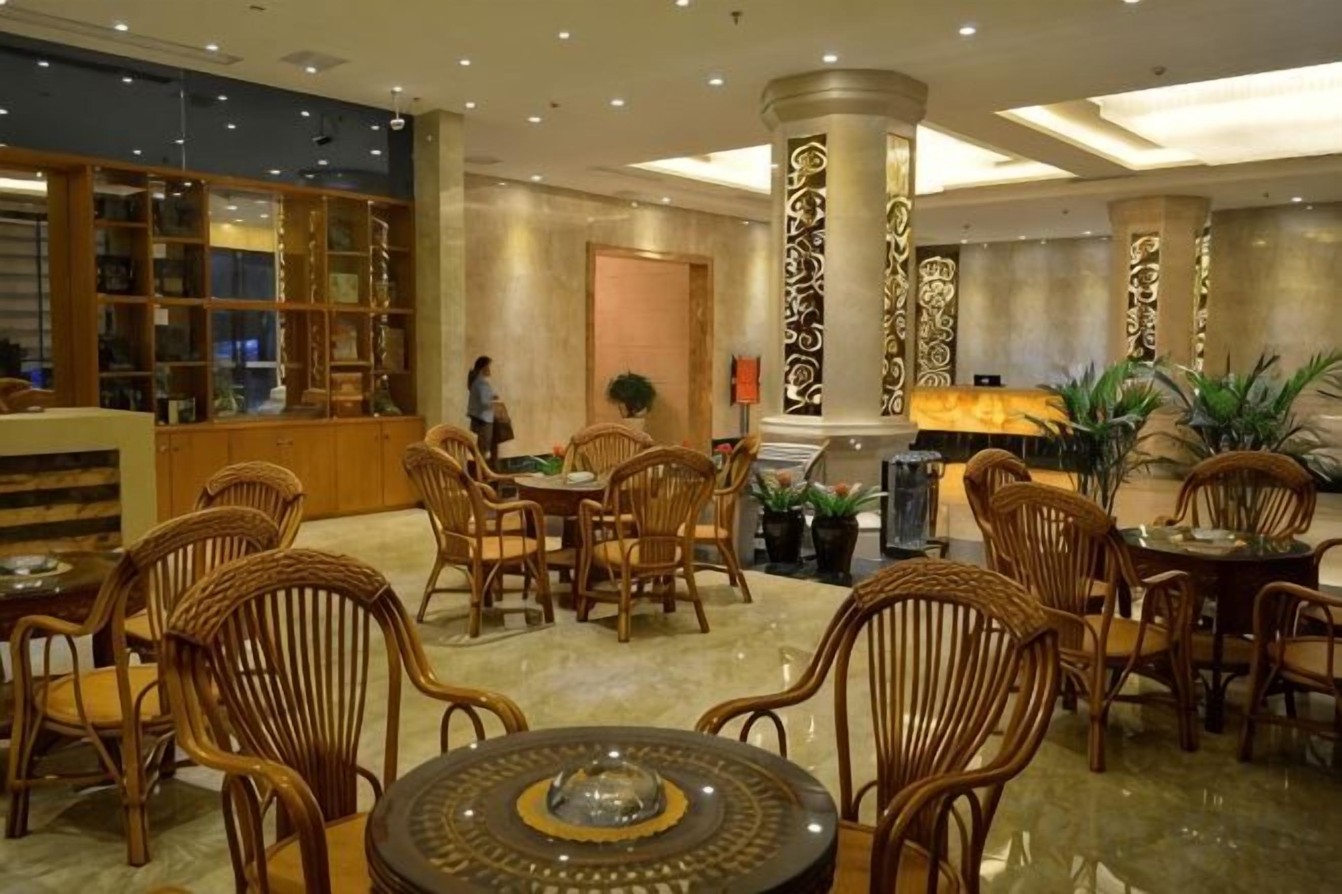 A hotel lobby with a reception desk, seating area with wicker chairs, and a decorative column.