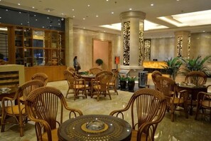 Un hall d’hôtel comprenant un comptoir d’accueil, un espace salon avec des fauteuils en osier et une colonne décorative.