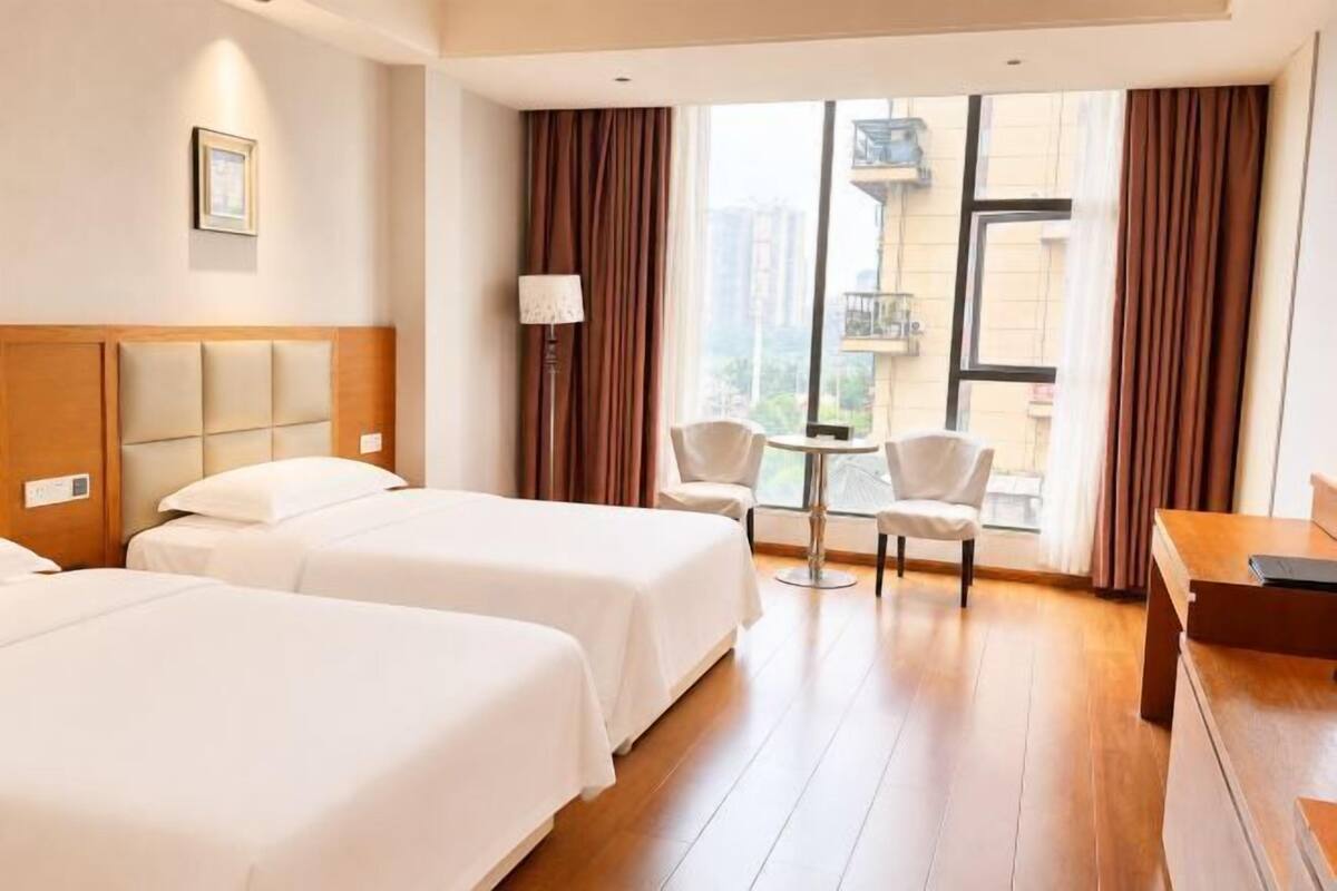 Een hotelkamer met twee bedden, een kleine tafel, een stoel en een raam met gordijnen.