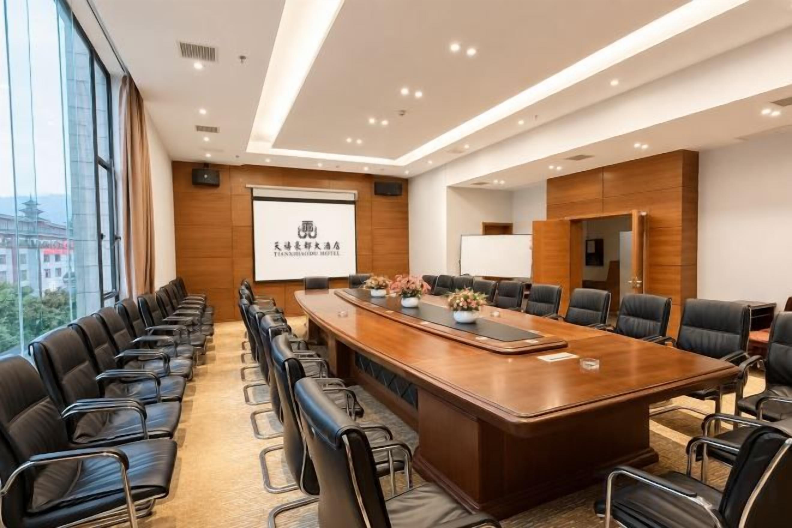Un salón de conferencias con una mesa larga, sillas negras y una pantalla para proyector.