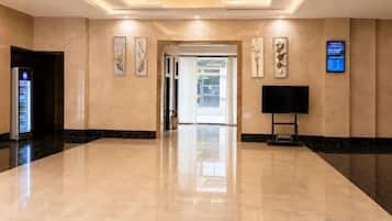 A hotel lobby with a marble floor, a reception desk, a television, and framed artwork on the walls.