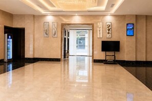 A hotel lobby with a marble floor, a reception desk, a television, and framed artwork on the walls.