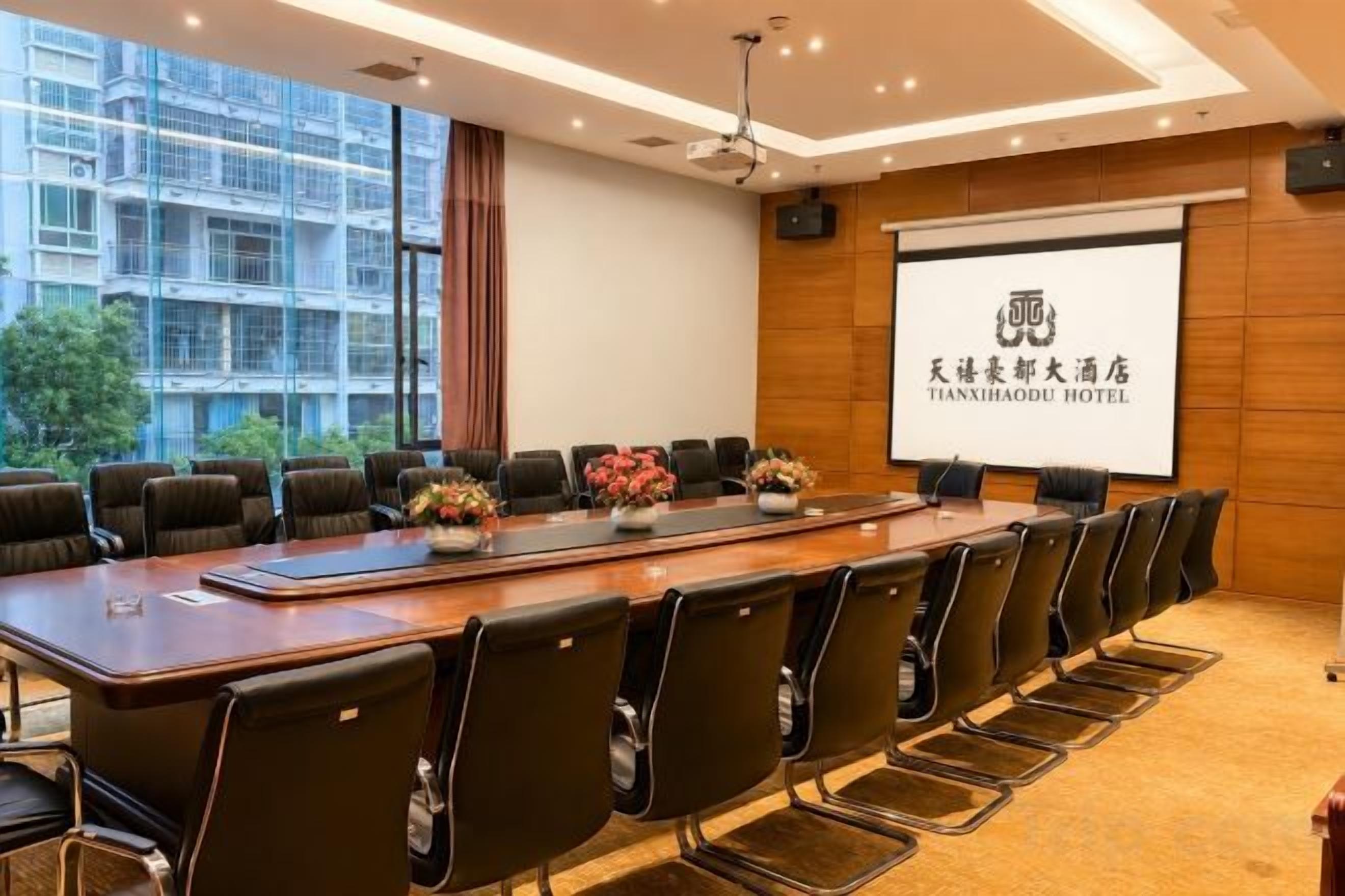 A conference room with a long table, chairs, and a projector screen displaying hotel branding.