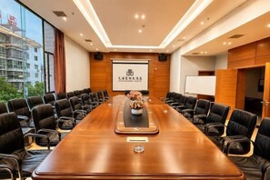 Une salle de conférence avec une longue table, des fauteuils en cuir noir, un écran de projection et un arrangement floral en guise de décoration centrale.