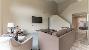 A living room with a sofa, a coffee table, a TV mounted on the wall, and a staircase leading to another room.