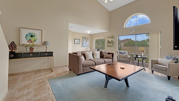 A spacious living room with a large coffee table, sofas, and a TV. There is a window with a view of the outdoors.