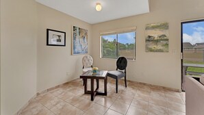 A room with a dining table and two chairs, a ceiling light, and three framed artworks on the walls.