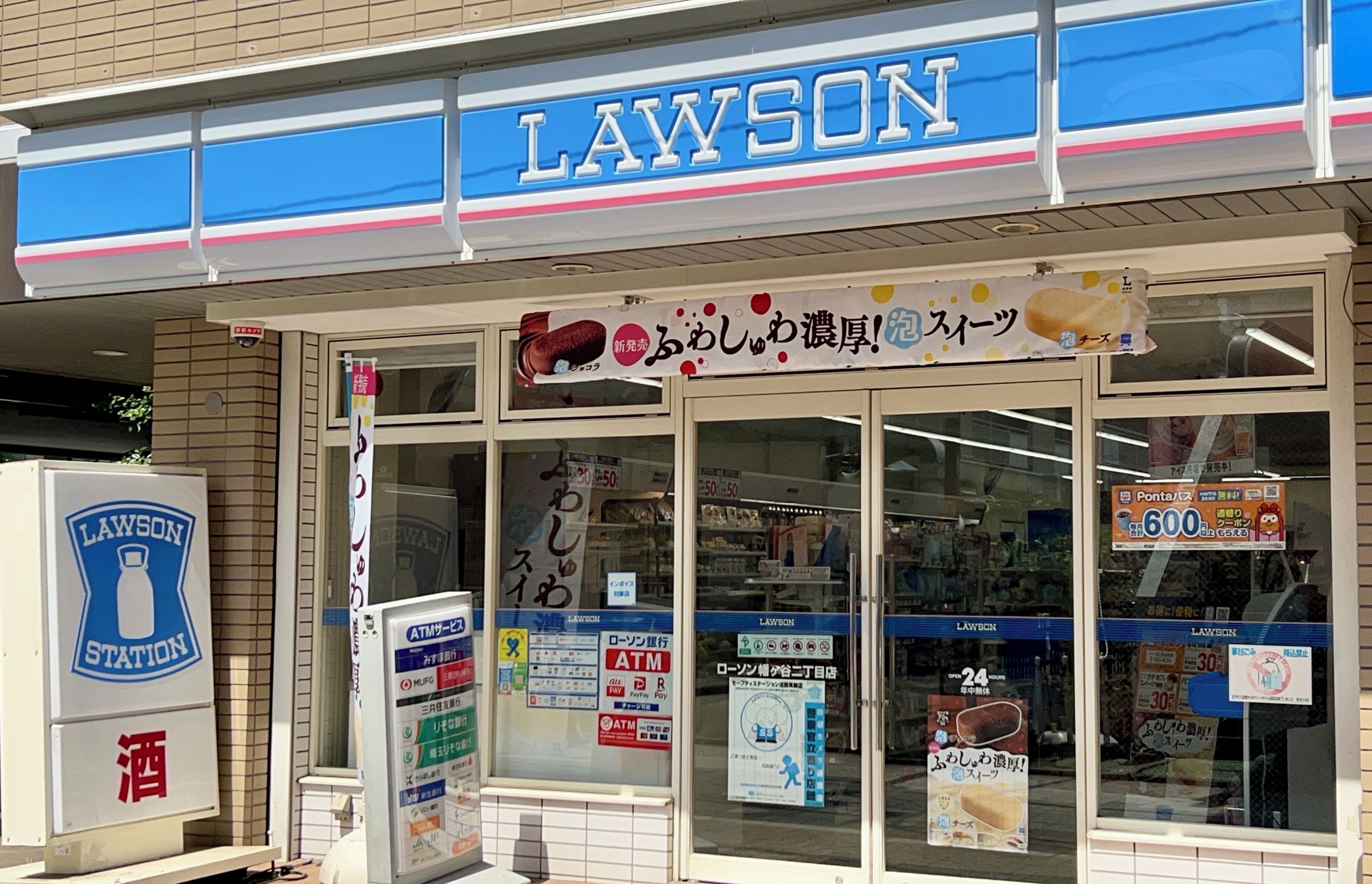 A Lawson convenience store with a blue and white sign, an ATM, and various promotional posters.