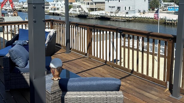 En træterrasse med fletmøbler, gelænder og udsigt til huse og en bro.
