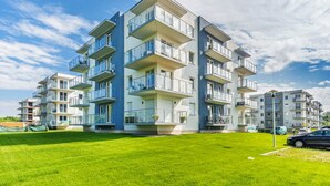 Un immeuble résidentiel à plusieurs étages, doté de balcons, d’une pelouse bien entretenue et surplombant un ciel bleu dégagé.
