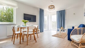 Un salon moderne comprenant un coin repas, un téléviseur et une grande fenêtre agrémentée de rideaux.
