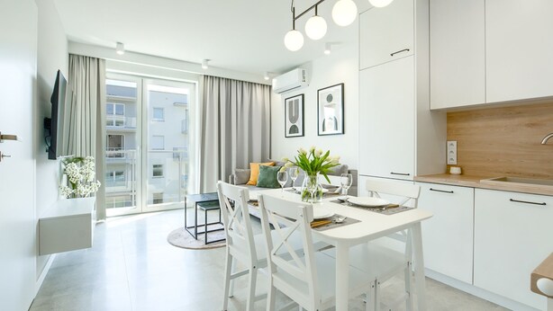 Un appartement moderne et bien éclairé, comprenant un coin repas, une cuisine et un balcon agrémenté de rideaux.