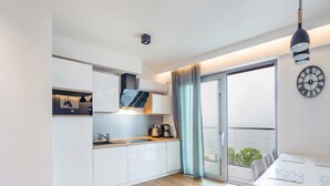 Een moderne keuken met witte kasten, een houten aanrechtblad en een ingebouwde oven. Er is een eethoek met een tafel en stoelen, en een groot raam met uitzicht op de omgeving.