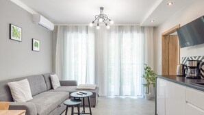 Una sala de estar moderna con un sofá gris, dos mesitas redondas, una cafetera y un televisor a la derecha.