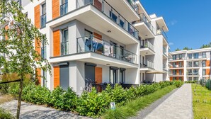 Un moderno edificio residencial de varios pisos, con balcones, un sendero pavimentado y un jardín bien cuidado.