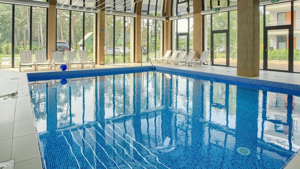 Una piscina interior con agua cristalina azul, rodeada de amplios ventanales y pilares de madera.