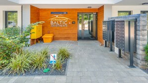 Una entrada moderna a un edificio con fachada de madera, un cartel de POBIEROWO BALTIC APARTMENTS y un buzón.