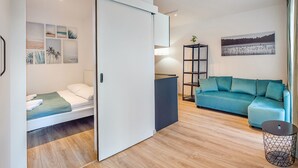 Un espacio habitable moderno y funcional con cama, sofá, una mesita y estantería.