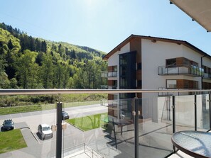 A modern building with a balcony, a glass railing, and a view of a road and greenery.