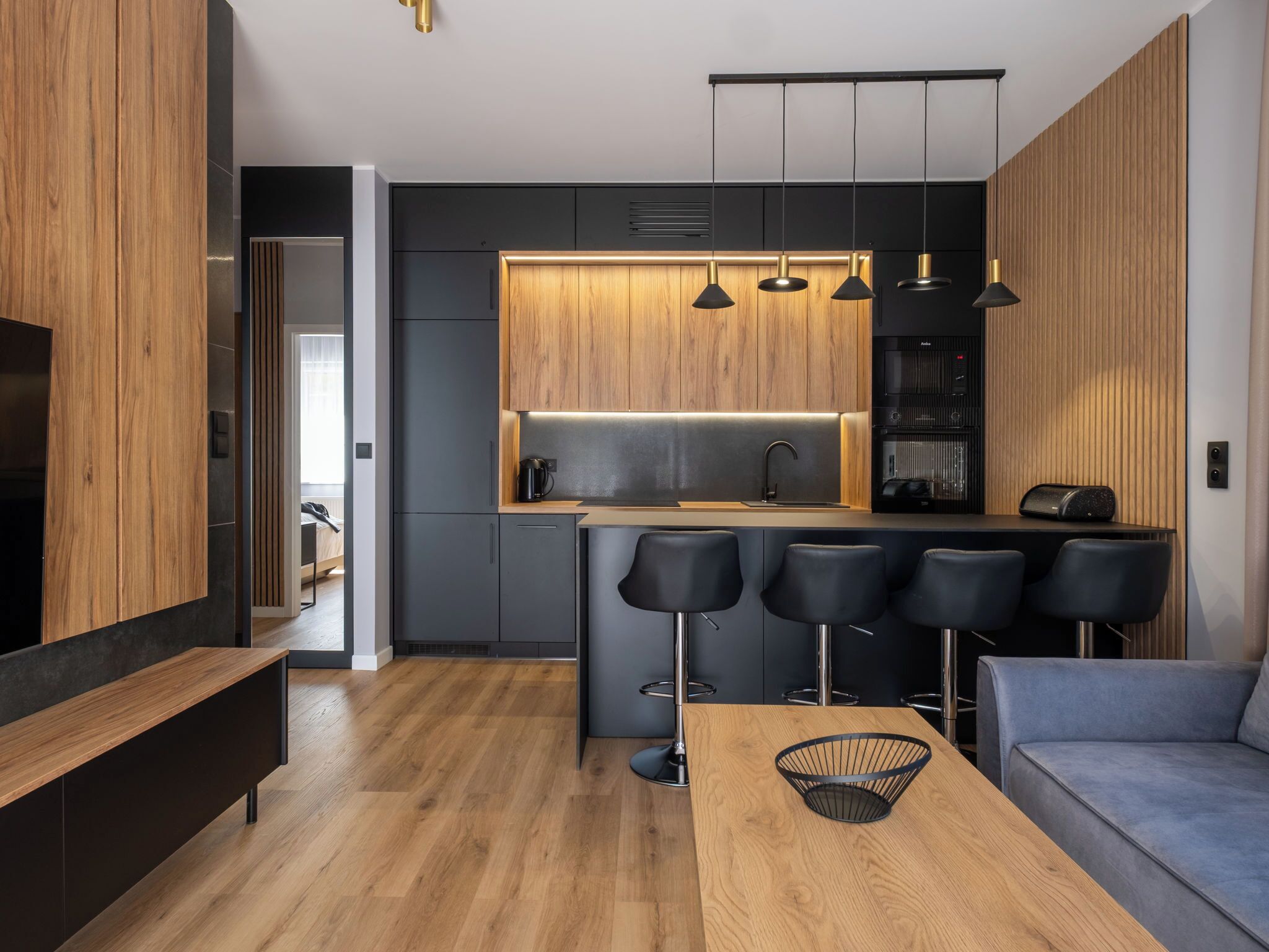 A modern kitchen with a wooden countertop, black bar stools, and pendant lights.