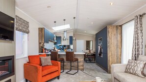 A modern living room with a fireplace, a dining area, and a kitchen with blue cabinets and a wooden accent wall.