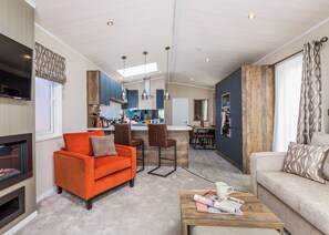 A modern living room with a fireplace, a dining area, and a kitchen with blue cabinets and a wooden accent wall. - Luxurious Lodge, perfect for couples or familes, sleeping four people. (Nr Kintore)