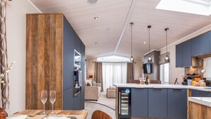 Una cuina moderna amb una illa central, zona de menjador amb taula per a dues persones, i espai de sala d'estar amb sofà.
