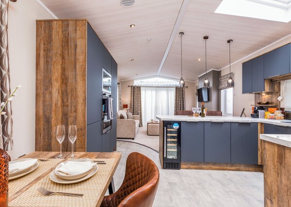 A modern kitchen with a central island, dining area with a table set for two, and a living space with a sofa. - Luxurious Lodge, perfect for couples or familes, sleeping four people. (Nr Kintore)