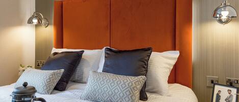A neatly made bed with a headboard, pillows, a bedside table with a lamp, and a picture frame on the nightstand.