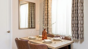 A dining area with a table set for six, a vase with branches, and a mirror on the wall.
