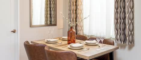 Un comedor con una mesa dispuesta para seis, un florero con ramas y un espejo en la pared.