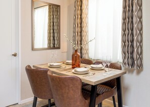 A dining area with a table set for six, a vase with branches, and a mirror on the wall. - Luxurious Lodge, perfect for couples or familes, sleeping four people. (Nr Kintore)