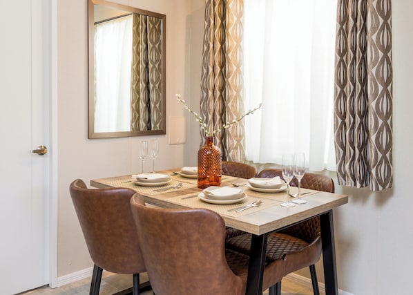 A dining area with a table set for six, a vase with branches, and a mirror on the wall. - Luxurious Lodge, perfect for couples or familes, sleeping four people. (Nr Kintore)