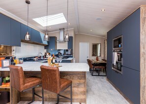 A modern kitchen with a central island, bar stools, a dining area, and built-in appliances. - Luxurious Lodge, perfect for couples or familes, sleeping four people. (Nr Kintore)