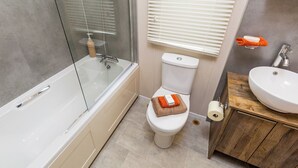 Un bany modern amb plat de dutxa inclòs en vidre, un vàter i un lavabo.
