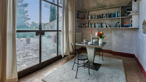 Una habitación con un ventanal grande, una mesa con sillas, una estantería y un radiador.