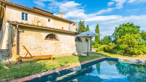 Vista de una piscina junto a una casa, con un banco y un pequeño pabellón.