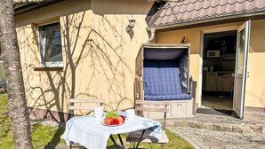 A small outdoor dining area with a table set for two, a cushioned bench, and a kitchen visible through an open door. - Dat lütt Huus by Interhome (Zinnowitz)