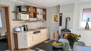 A modern kitchen with a dishwasher, microwave, and oven. There is a dining table with a fruit bowl and a vase of flowers. - Dat lütt Huus by Interhome (Zinnowitz)