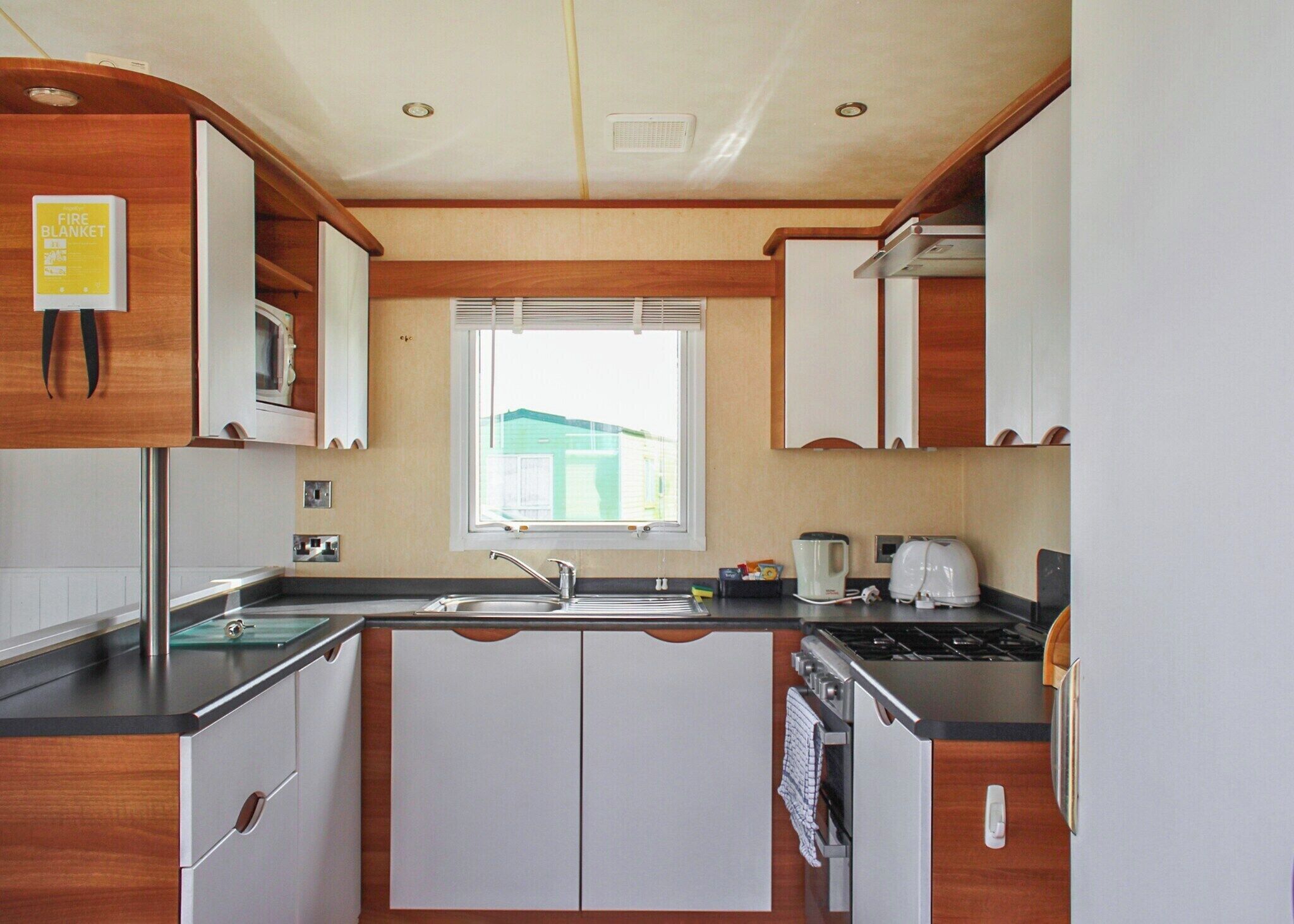 A compact kitchen with white cabinets, a built-in stove, a sink, and a window with a view of a house.